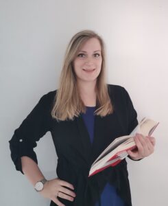 Nina Kainz hält ein aufgeschlagenes Wörterbuch in der Hand und lächelt in die Kamera